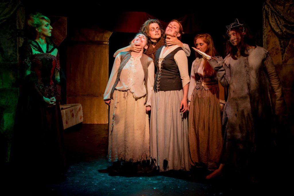 Helena Jo (Kaelea Rovinsky) threatens both Susannah (Juliana Brecher) and Kate (Aiyanna Wade), observed by Elizabeth Bathory (Mary-Kate Arnold), new recruit Jane (Lana Whittington), and Erzi the Witch (Katy Jenkins)